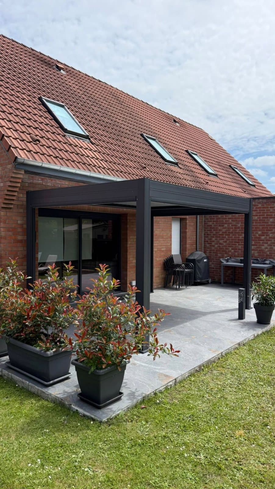 Pergola bioclimatique autoportante anthracite sur une terrasse carrelée devant une maison en briques