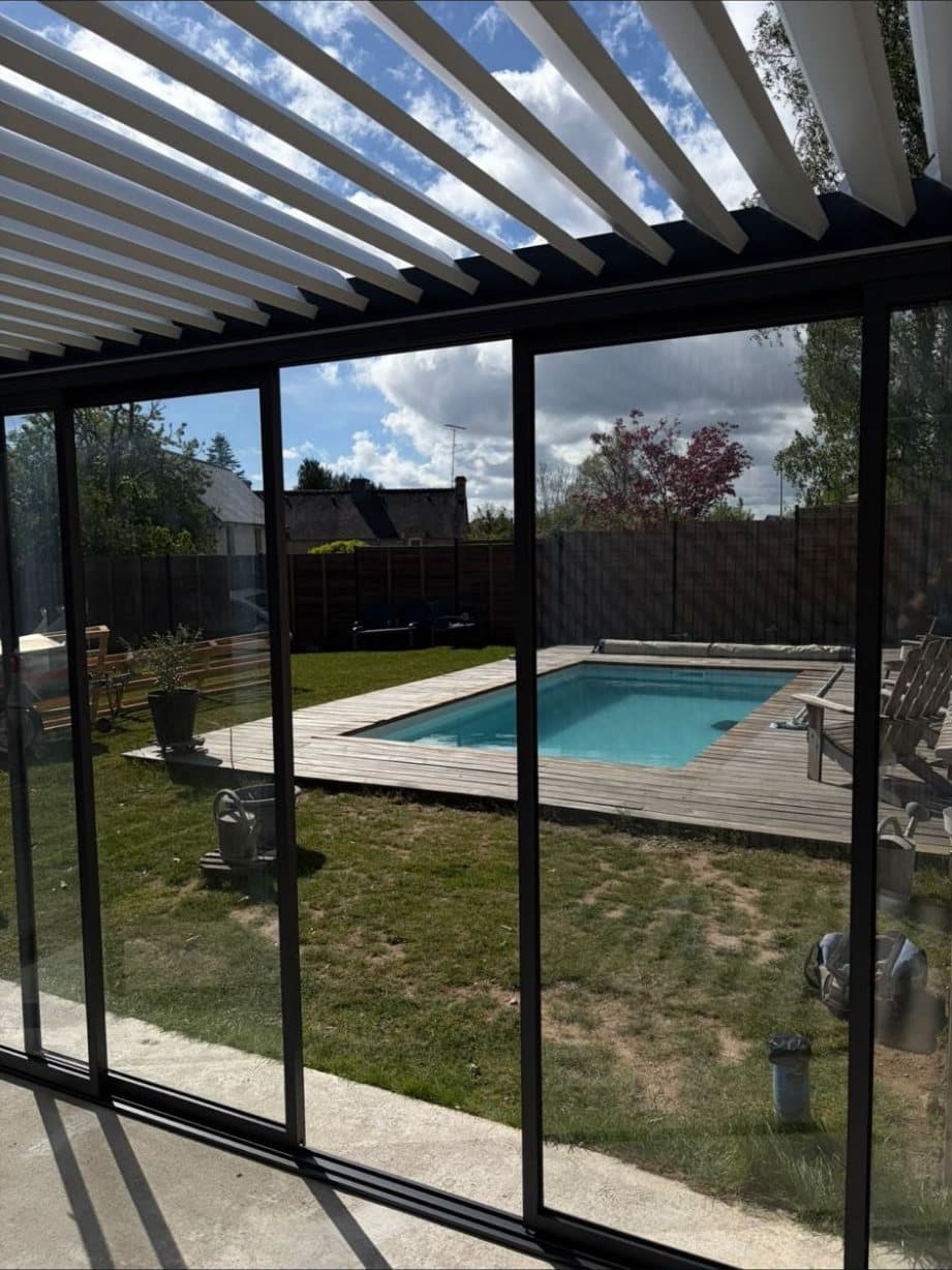 Lames orientables d'une pergola bioclimatique ouvertes vers le ciel, avec vue sur une piscine à travers les vitrages