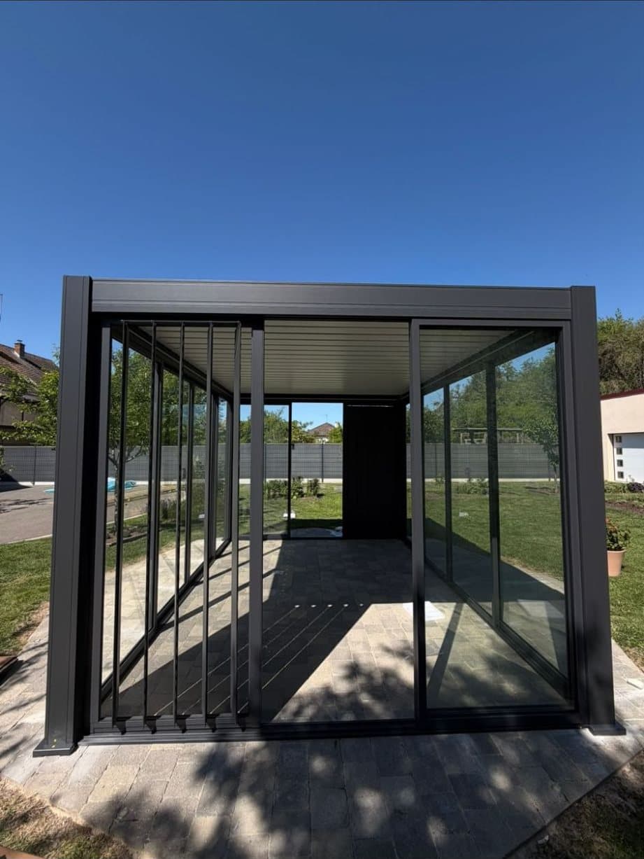 Pergola bioclimatique autoportante vue de face, avec vitrages coulissants, lames orientables et ciel bleu